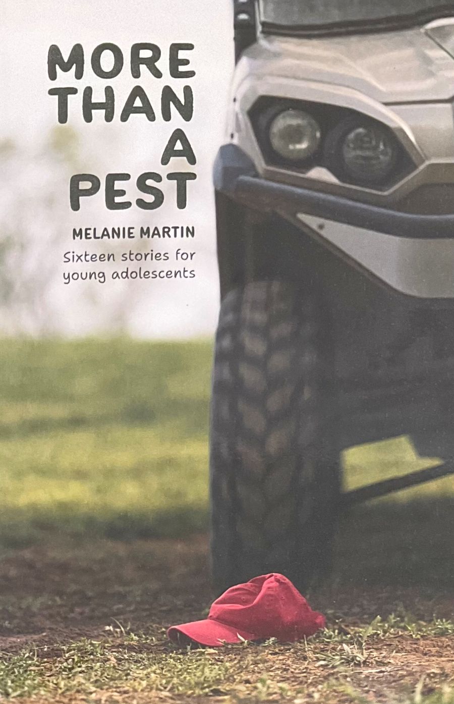 Book cover for 'More Than a Pest' by Melanie Martin, featuring a close-up of a vehicle tire and front bumper with a red cap on the ground in the foreground.